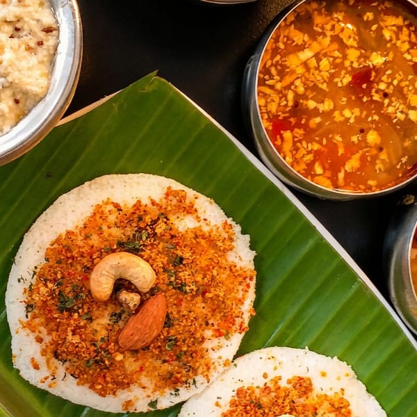 South Indian idlis on a banana leaf, topped with spices and nuts, served with three chutneys.