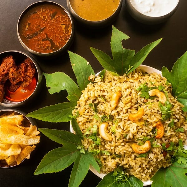 Indian biryani with cashews and herbs, accompanied by various curries and crispy snacks.