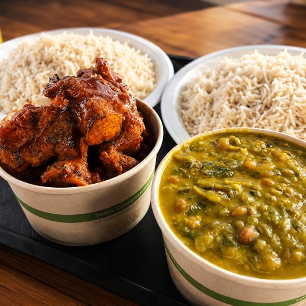 A tray with two plates of rice, a bowl of chicken curry, and a bowl of green stew.